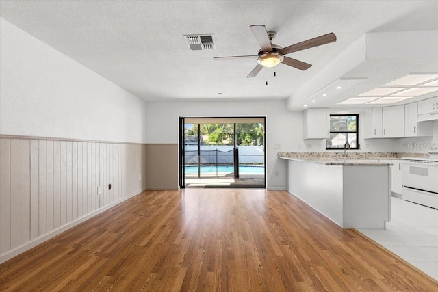 2233 Curlew Rd, Dunedin, FL 34698 - kitchen with electric stove, light wood-type flooring, open floor plan, white cabinets, and wainscoting