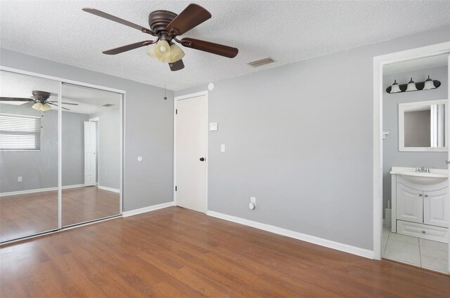 1806 11th St SW, Largo, FL 33778 - unfurnished bedroom featuring wood finished floors, a textured ceiling, a ceiling fan, connected bathroom, and a closet