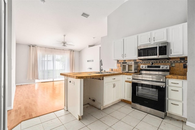 10039 Creek Bluff Dr, Riverview, FL 33578 - kitchen featuring stainless steel appliances, a peninsula, vaulted ceiling, decorative backsplash, and white cabinetry