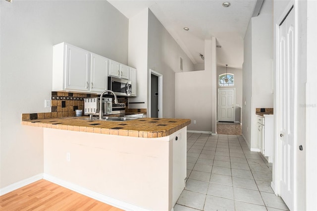 10039 Creek Bluff Dr, Riverview, FL 33578 - kitchen with stainless steel microwave, a peninsula, decorative backsplash, white cabinetry, and light tile patterned floors