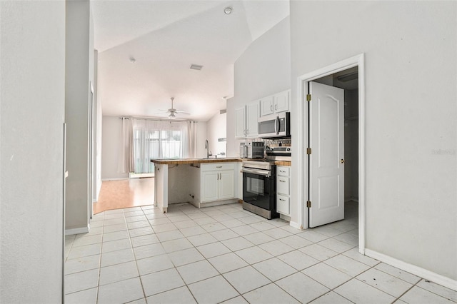 10039 Creek Bluff Dr, Riverview, FL 33578 - kitchen featuring appliances with stainless steel finishes, a peninsula, white cabinets, light tile patterned floors, and high vaulted ceiling