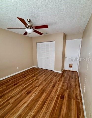 5110 Corvette Dr, Tampa, FL 33624 - unfurnished bedroom featuring wood finished floors, a textured ceiling, a closet, and a ceiling fan