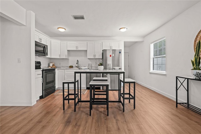 1743 Fulton Ave, Clearwater, FL 33755 - kitchen featuring appliances with stainless steel finishes, white cabinetry, tasteful backsplash, and light wood-style flooring