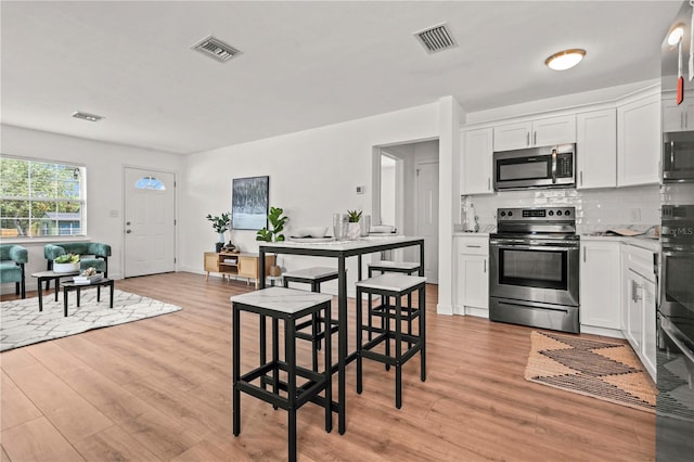 1743 Fulton Ave, Clearwater, FL 33755 - kitchen featuring appliances with stainless steel finishes, light wood finished floors, white cabinets, and backsplash