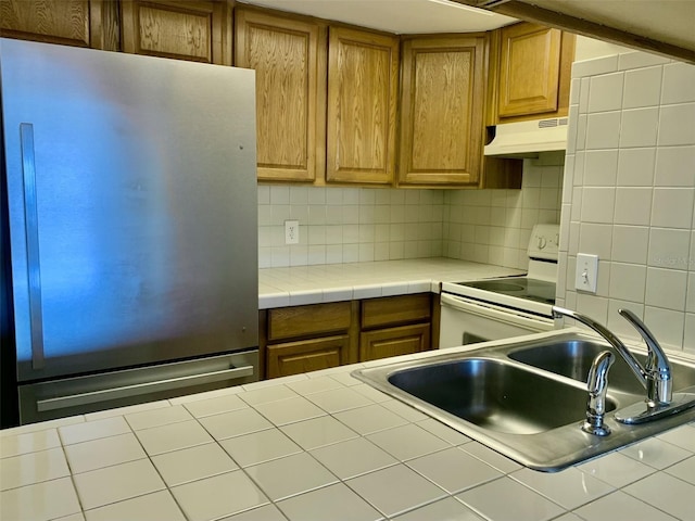 4712 Marine Pkwy Unit 203, New Port Richey, FL 34652 - kitchen featuring freestanding refrigerator, white electric range oven, under cabinet range hood, backsplash, and brown cabinetry