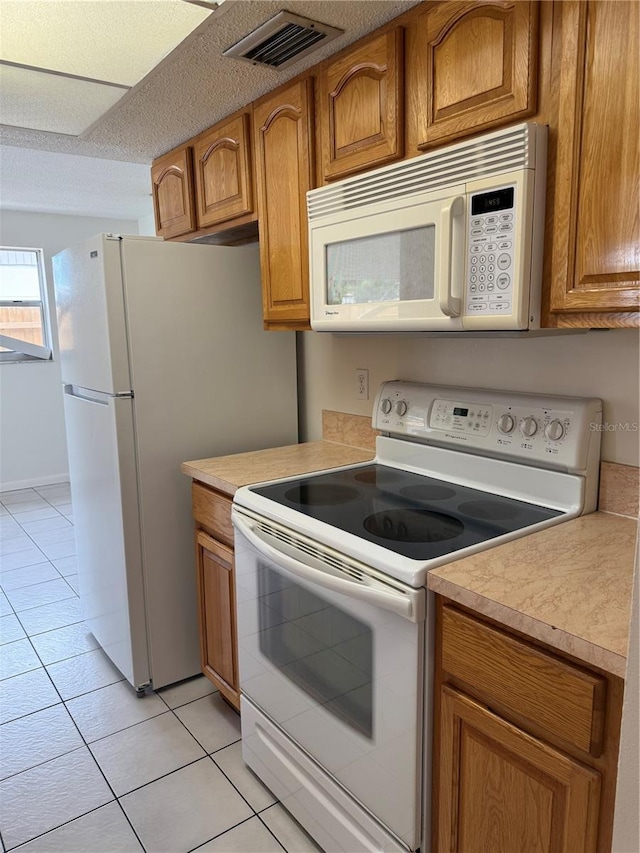 8801 Orange Blossom Dr, Seminole, FL 33772 - kitchen featuring white appliances, light tile patterned floors, light countertops, and brown cabinets
