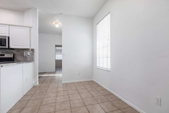 5017 46th St W, Bradenton, FL 34210 - kitchen featuring stainless steel microwave, white cabinetry, tasteful backsplash, light tile patterned floors, and a textured ceiling
