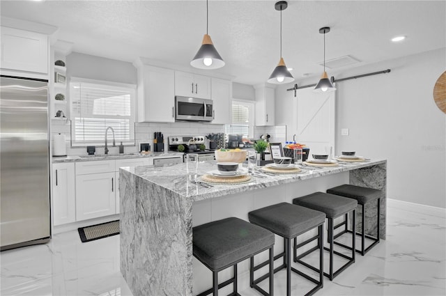 8010 W Hiawatha St, Tampa, FL 33615 - kitchen featuring appliances with stainless steel finishes, a barn door, backsplash, light marble finish floors, and a kitchen island