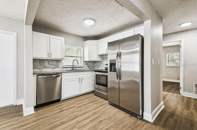 10215 N 23rd St, Tampa, FL 33612 - kitchen with stainless steel appliances, light wood finished floors, decorative backsplash, white cabinetry, and a textured ceiling