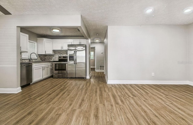 10215 N 23rd St, Tampa, FL 33612 - kitchen with stainless steel appliances, wood finished floors, a textured ceiling, white cabinetry, and decorative backsplash