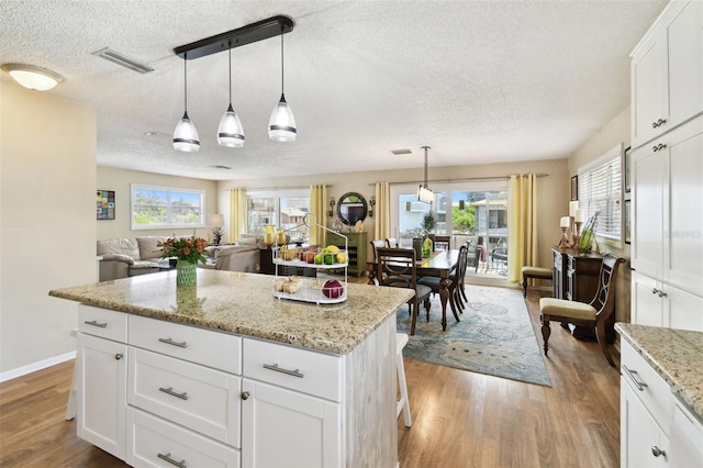 616 2nd St, Indian Rocks Beach, FL 33785 - kitchen featuring a textured ceiling, wood finished floors, light stone countertops, hanging light fixtures, and open floor plan