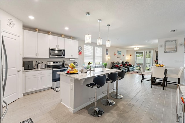 39024 Harlow Rose Dr, Zephyrhills, FL 33540 - kitchen featuring appliances with stainless steel finishes, light wood-type flooring, an island with sink, a kitchen breakfast bar, and white cabinets