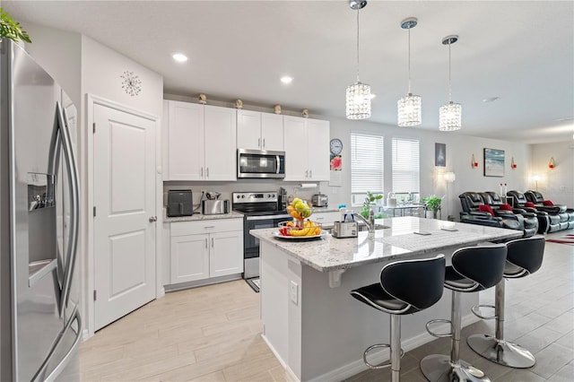 39024 Harlow Rose Dr, Zephyrhills, FL 33540 - kitchen featuring appliances with stainless steel finishes, a kitchen breakfast bar, light wood-style floors, white cabinetry, and recessed lighting