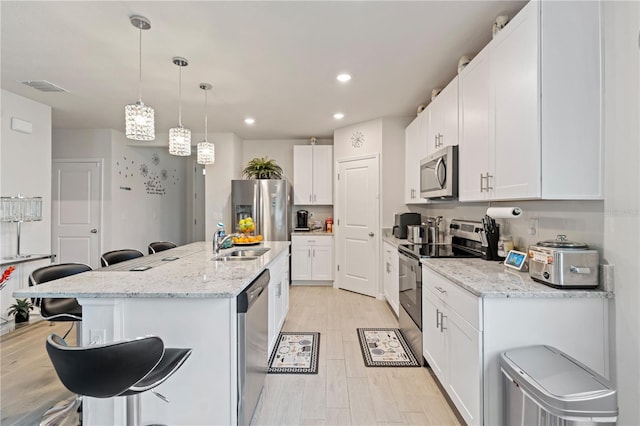 39024 Harlow Rose Dr, Zephyrhills, FL 33540 - kitchen with appliances with stainless steel finishes, a breakfast bar, light wood-style floors, white cabinets, and recessed lighting