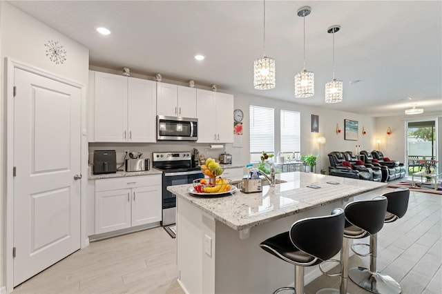 39024 Harlow Rose Dr, Zephyrhills, FL 33540 - kitchen featuring stainless steel appliances, white cabinets, a center island, a breakfast bar, and light wood-style floors