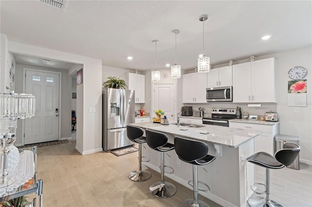 39024 Harlow Rose Dr, Zephyrhills, FL 33540 - kitchen with stainless steel appliances, light wood-style floors, a breakfast bar area, white cabinetry, and recessed lighting