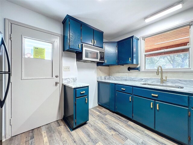 1938 E Fern Rd, Lakeland, FL 33801 - kitchen with white microwave, blue cabinetry, light countertops, light wood finished floors, and freestanding refrigerator
