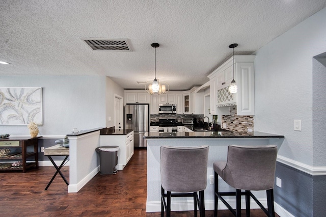 3173 Fountainhead Dr, Largo, FL 33770 - kitchen with stainless steel appliances, a peninsula, a textured ceiling, glass insert cabinets, and dark countertops