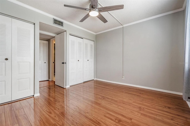 2901 W 26th St Unit 301, Bradenton, FL 34205 - unfurnished bedroom with multiple closets, light wood-style flooring, a textured ceiling, ornamental molding, and a ceiling fan