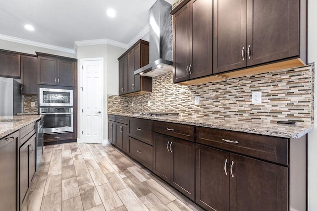 21675 Amelia Rose Way, Land O Lakes, FL 34637 - kitchen with wall chimney range hood, stainless steel appliances, dark brown cabinetry, ornamental molding, and light stone counters