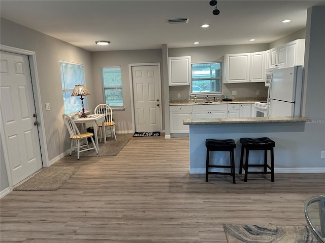 7651 46th Way N, Pinellas Park, FL 33781 - kitchen featuring white appliances, white cabinets, a peninsula, a kitchen breakfast bar, and light wood finished floors