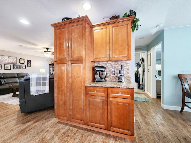 8110 Damara Dr, New Port Richey, FL 34653 - kitchen featuring light wood-style floors, tasteful backsplash, light stone countertops, ceiling fan, and brown cabinets