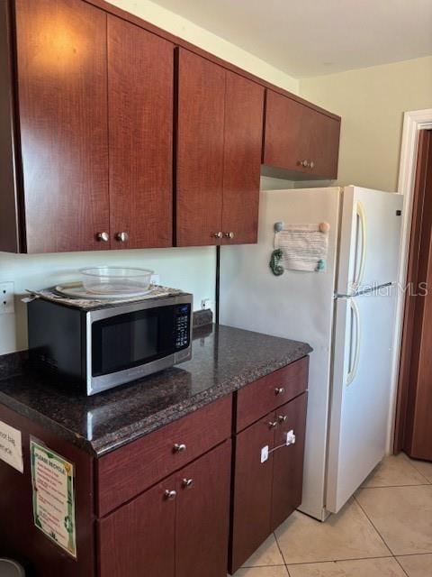 1021 16th Ave SW, Largo, FL 33770 - kitchen featuring stainless steel microwave, light tile patterned floors, dark stone countertops, and freestanding refrigerator