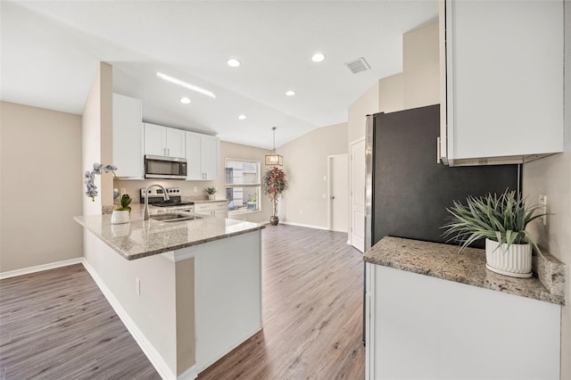 5131 Gato Del Sol Cir, Wesley Chapel, FL 33544 - kitchen with stainless steel microwave, light stone counters, light wood-style flooring, white cabinets, and a peninsula