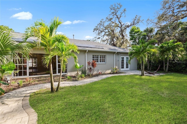 302 Eastleigh Dr, Belleair, FL 33756 - rear view of house featuring french doors, a lawn, solar panels, stucco siding, and a patio area
