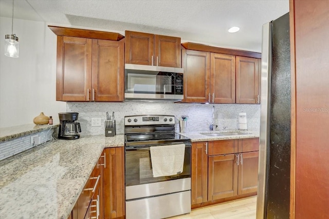 2078 Sunset Point Rd Unit 83, Clearwater, FL 33765 - kitchen featuring stainless steel appliances, decorative backsplash, light stone counters, brown cabinets, and pendant lighting