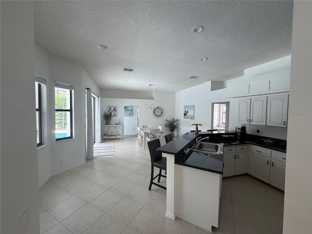 199 N Crystal Meadow Path, Lecanto, FL 34461 - kitchen with a textured ceiling, a peninsula, dark countertops, a kitchen bar, and light tile patterned floors