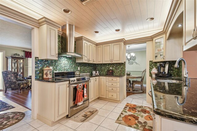 9548 141st St, Seminole, FL 33776 - kitchen with stainless steel range with electric cooktop, cream cabinetry, wall chimney exhaust hood, crown molding, and light tile patterned flooring