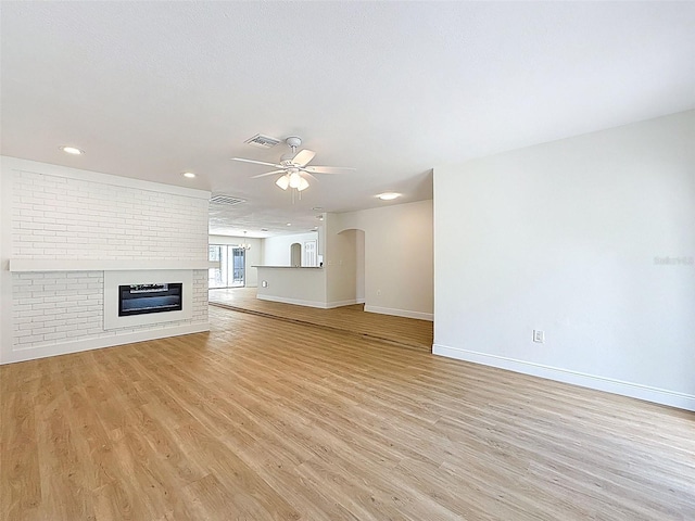 603 Ivey Ln, Tarpon Springs, FL 34689 - unfurnished living room featuring a ceiling fan, light wood-style flooring, a brick fireplace, recessed lighting, and arched walkways