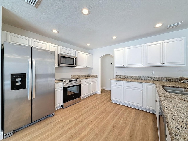 603 Ivey Ln, Tarpon Springs, FL 34689 - kitchen featuring appliances with stainless steel finishes, light wood-type flooring, arched walkways, white cabinets, and recessed lighting