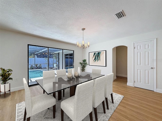 603 Ivey Ln, Tarpon Springs, FL 34689 - dining room with arched walkways, a textured ceiling, light wood-type flooring, and a chandelier