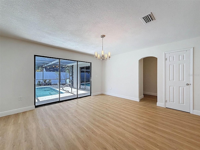 603 Ivey Ln, Tarpon Springs, FL 34689 - unfurnished room with a textured ceiling, light wood-style flooring, arched walkways, and a chandelier