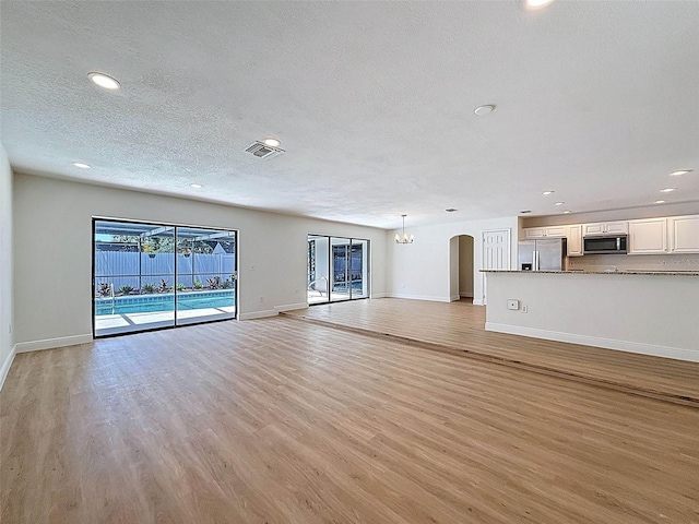 603 Ivey Ln, Tarpon Springs, FL 34689 - unfurnished living room with a textured ceiling, light wood-style floors, recessed lighting, and arched walkways