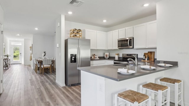 4338 Sand Dollar Way, Zephyrhills, FL 33541 - kitchen featuring appliances with stainless steel finishes, dark countertops, a peninsula, light wood-style flooring, and white cabinetry