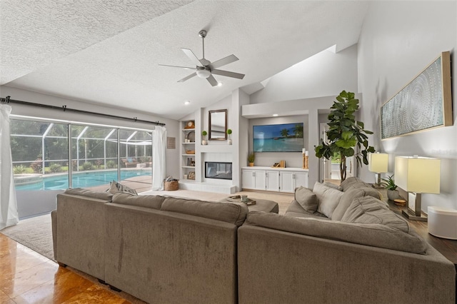 17311 Carriage Way, Odessa, FL 33556 - living room featuring ceiling fan, vaulted ceiling, a textured ceiling, a large fireplace, and built in shelves