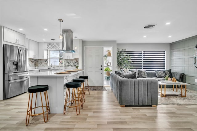 1384 S Hillcrest Ave, Clearwater, FL 33756 - kitchen with stainless steel fridge, island exhaust hood, light countertops, a breakfast bar area, and white cabinetry