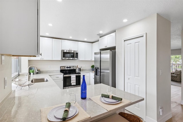 6521 Bimini Ct, Apollo Beach, FL 33572 - kitchen with appliances with stainless steel finishes, a peninsula, white cabinets, recessed lighting, and light stone counters