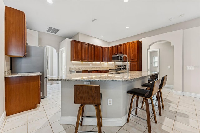 25946 Buckthorn Ave, Land O Lakes, FL 34639 - kitchen with stainless steel appliances, arched walkways, a breakfast bar, light stone countertops, and recessed lighting