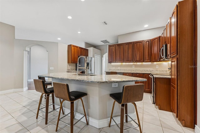25946 Buckthorn Ave, Land O Lakes, FL 34639 - kitchen featuring appliances with stainless steel finishes, a kitchen bar, arched walkways, light stone counters, and light tile patterned floors