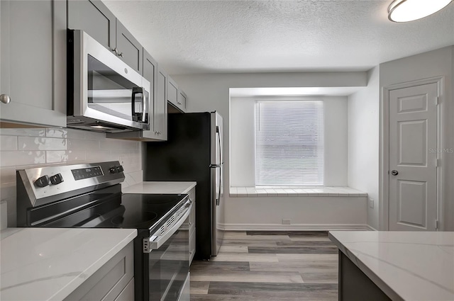4129 Marlow Loop, Land O Lakes, FL 34639 - kitchen featuring stainless steel appliances, light wood-style flooring, decorative backsplash, a textured ceiling, and gray cabinetry