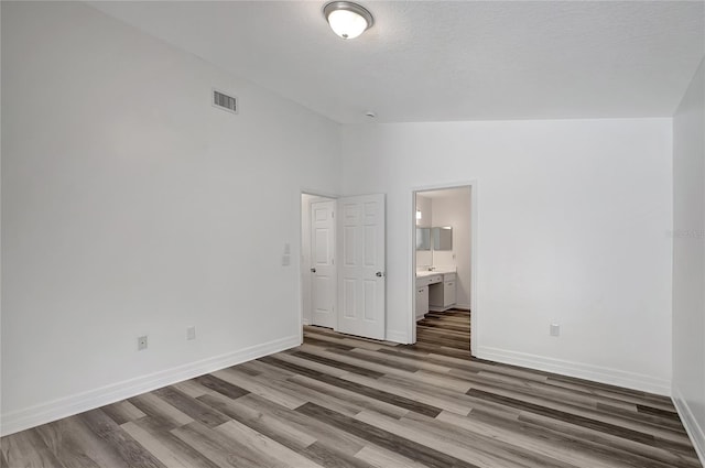 4129 Marlow Loop, Land O Lakes, FL 34639 - unfurnished bedroom featuring wood finished floors, vaulted ceiling, ensuite bathroom, and a textured ceiling