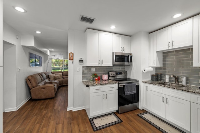 7003 Yule Ln, Tampa, FL 33637 - kitchen featuring appliances with stainless steel finishes, dark stone countertops, open floor plan, dark wood-style flooring, and white cabinets