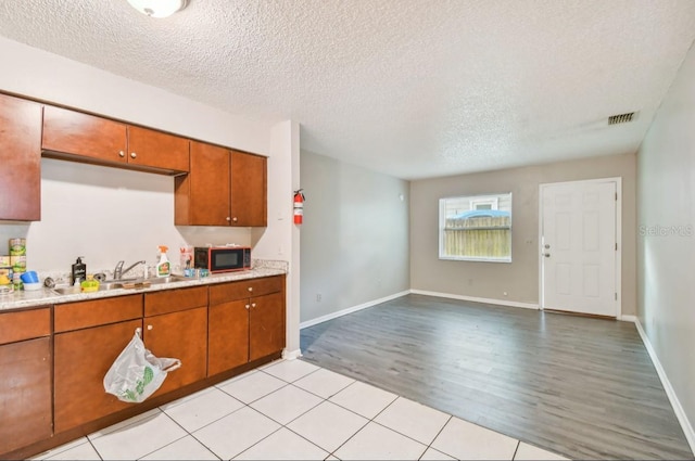 7920 N Marks St, Tampa, FL 33604 - kitchen featuring black microwave, a textured ceiling, light countertops, light wood-style flooring, and brown cabinets