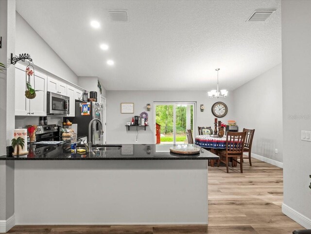 8737 N Spikes Way, Dunnellon, FL 34434 - kitchen with stainless steel appliances, a peninsula, white cabinets, light wood-style flooring, and a chandelier