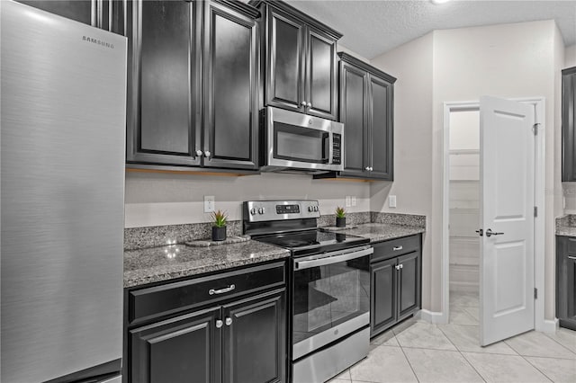 11308 Chilly Water Ct, Riverview, FL 33569 - kitchen with appliances with stainless steel finishes, dark cabinetry, light tile patterned flooring, stone countertops, and a textured ceiling