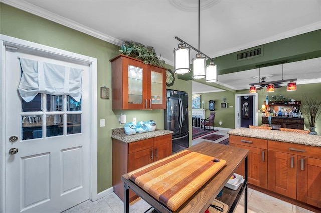 3898 49th Ave S, Saint Petersburg, FL 33711 - kitchen with freestanding refrigerator, ornamental molding, brown cabinetry, glass insert cabinets, and light stone countertops
